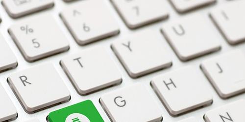 white computer keyboard with a green button with an arrow pointing down